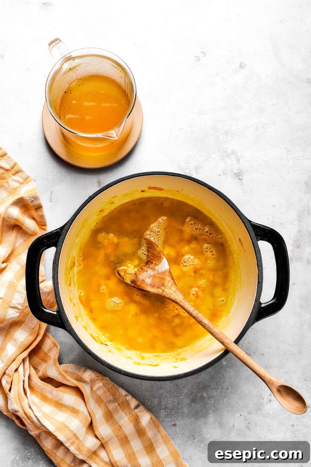 This easy broccoli cheddar soup recipe is packed with cozy flavor, featuring broccoli florets, diced potatoes, and freshly grated cheddar cheese. Stirring broth into a pot with carrots and roux.