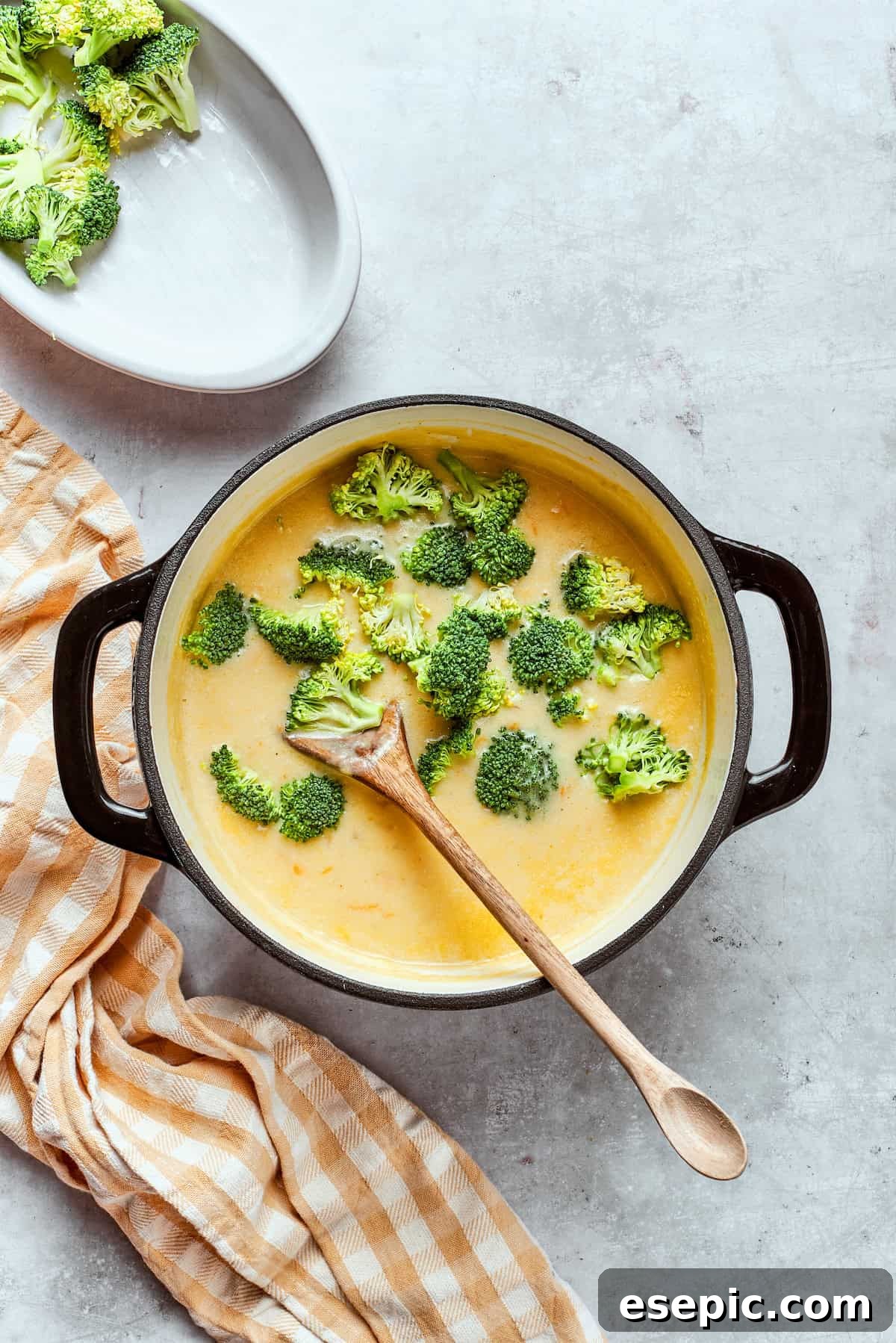 This easy broccoli cheddar soup recipe is packed with cozy flavor, featuring broccoli florets, diced potatoes, and freshly grated cheddar cheese. Stirring broccoli florets into a pot of soup.