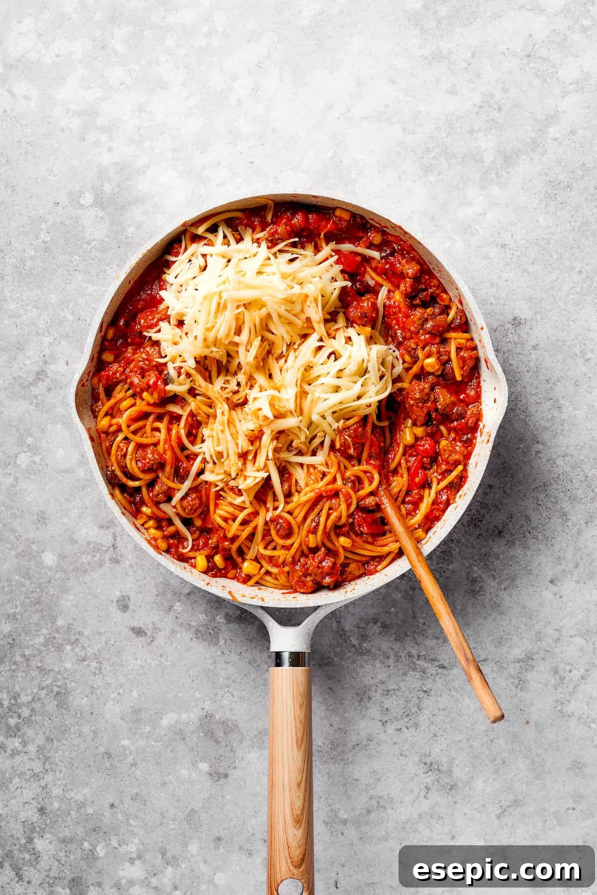 A generous amount of shredded Pepper Jack and Monterey Jack cheeses are sprinkled over the Mexican spaghetti in the pan, ready to melt into a creamy, gooey topping.