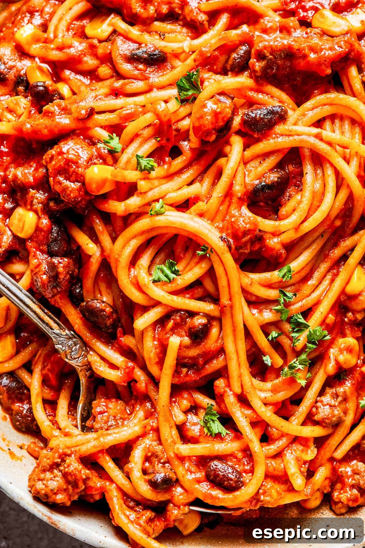A close-up view of Mexican spaghetti expertly tossed with a rich tomato and bean sauce, highlighting the texture and color of the ingredients.