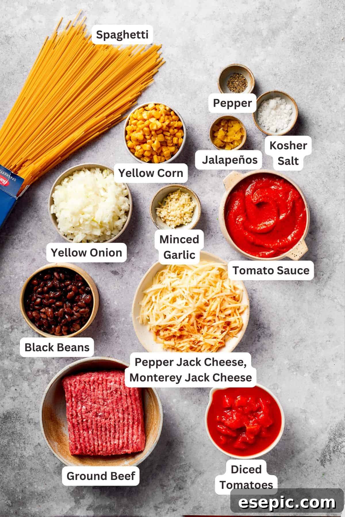 Various fresh and canned ingredients for Mexican taco spaghetti, including ground beef, diced tomatoes, black beans, corn, and cheese, all neatly arranged.