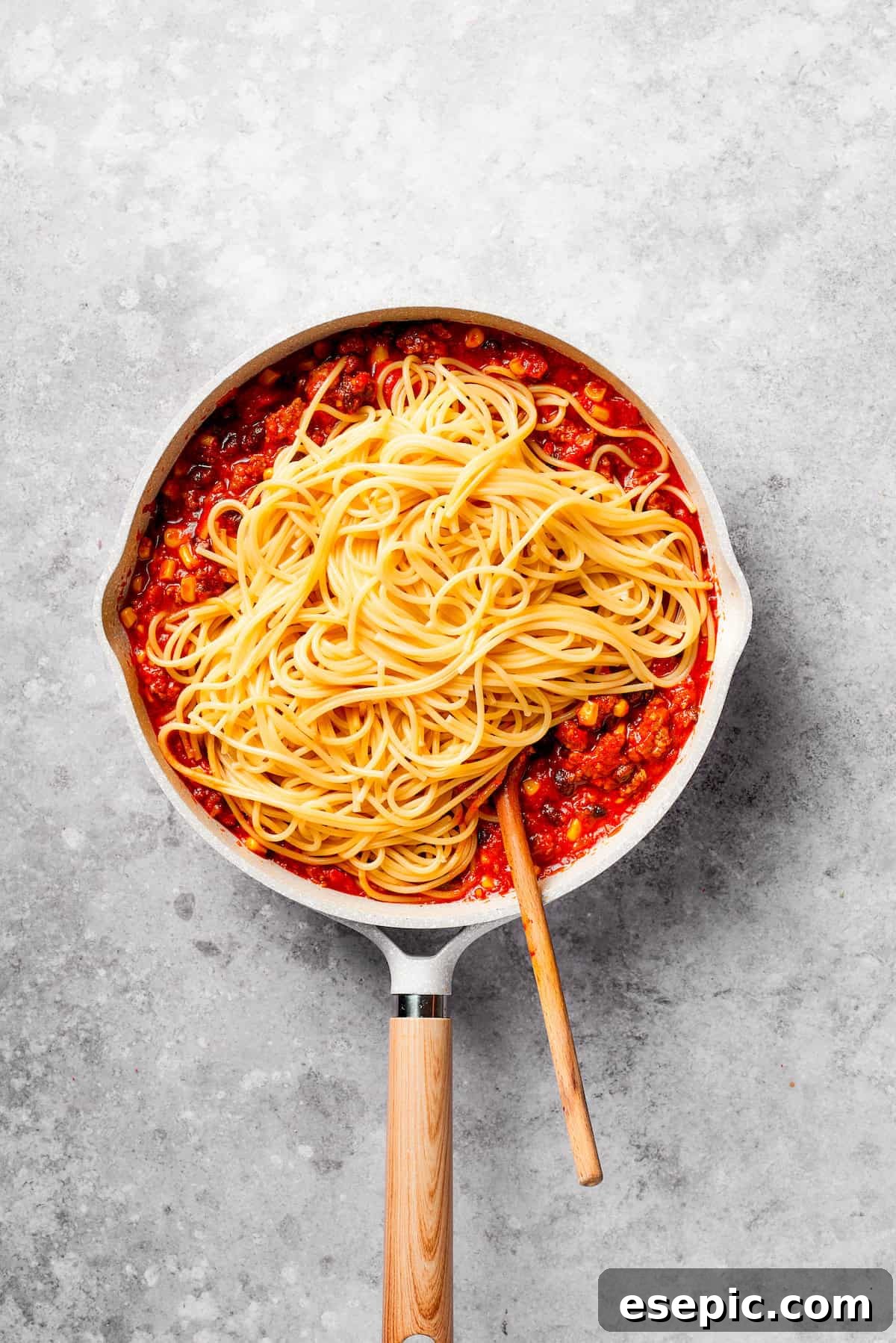 Perfectly cooked spaghetti strands are gently mixed into the rich, simmering Mexican-inspired meat sauce in a large pan, ensuring every strand is coated.