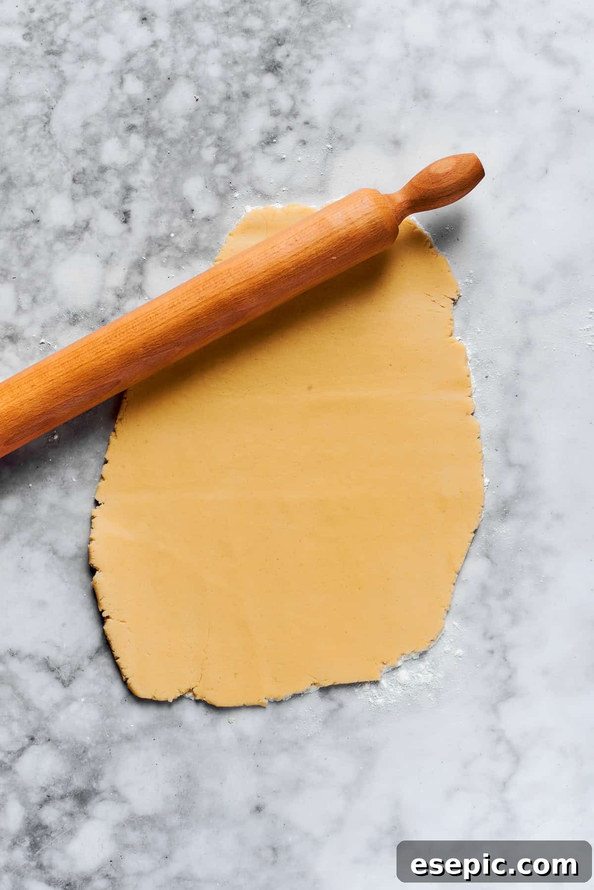 A rolling pin flattening sugar cookie dough on a floured surface to an even thickness.