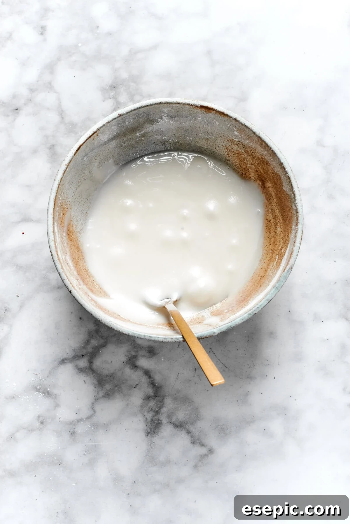 White icing being mixed in a bowl, achieving a smooth and spreadable consistency for frosting cookies.