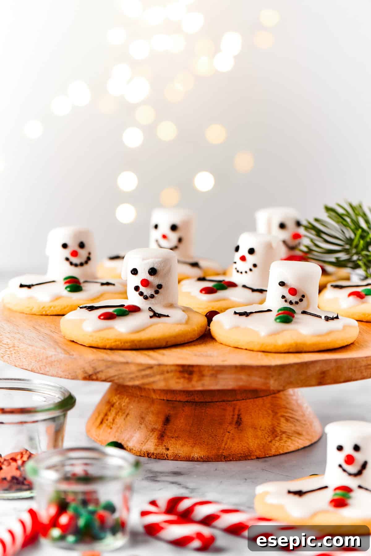 Melted snowman cookies artistically arranged on a wooden cake plate, surrounded by charming holiday decorations.