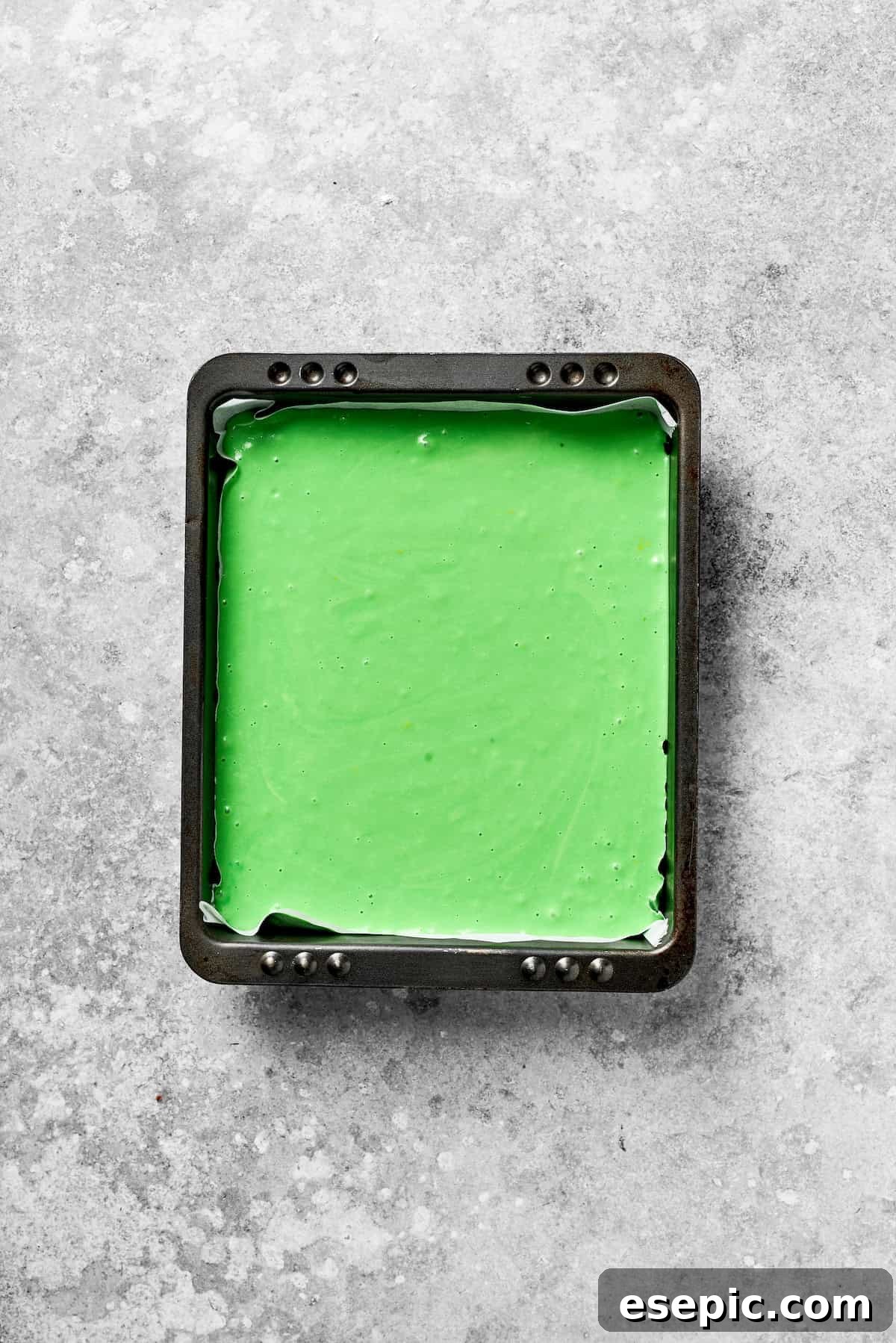 A square pan filled with vibrant green cake batter, ready for baking.