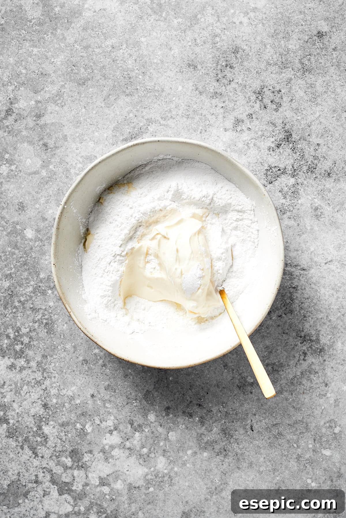 Cream cheese and powdered sugar mixed together in a bowl, forming a smooth base for the frosting.