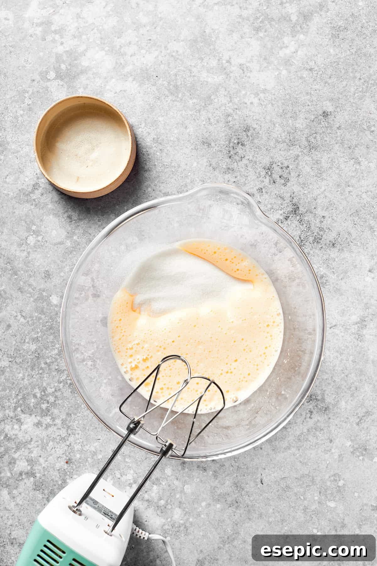 Granulated sugar being beaten into eggs, creating a light and fluffy mixture.