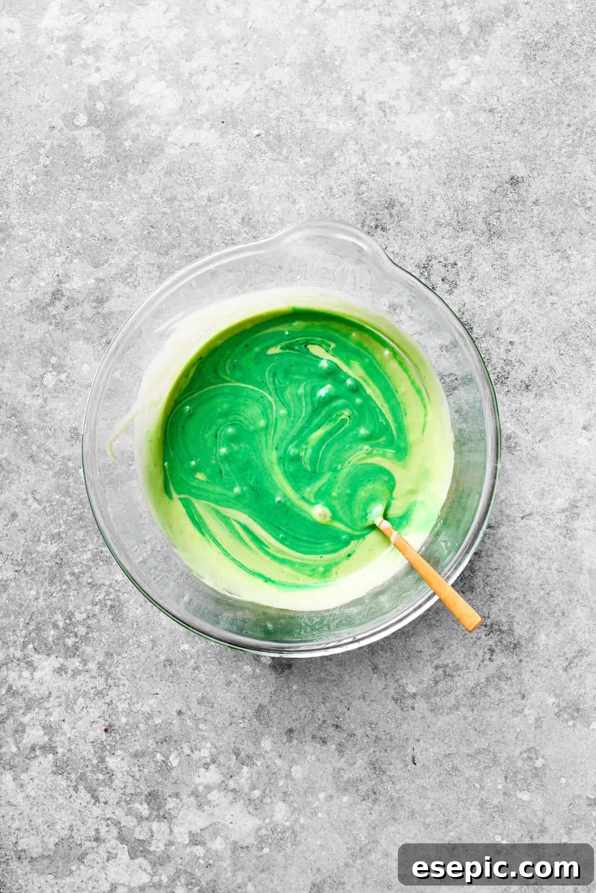 The grinch cake batter turns vibrant green as food coloring is stirred in.