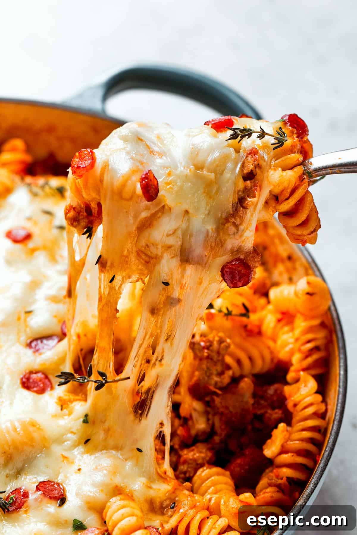 Pulling a serving of cheesy pizza pasta out of a baking dish, showing a long cheese pull.