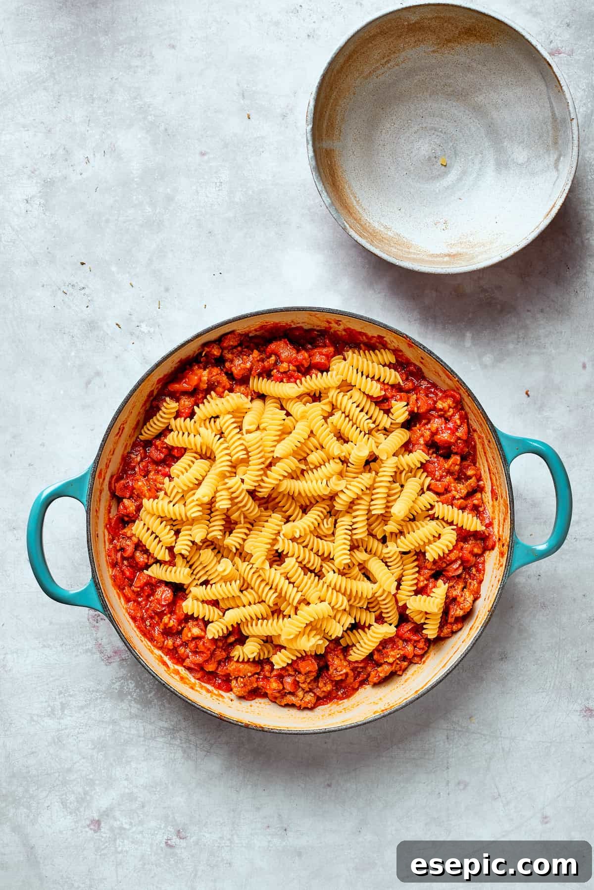 Pasta is added to a pan of sauce, ready for simmering.