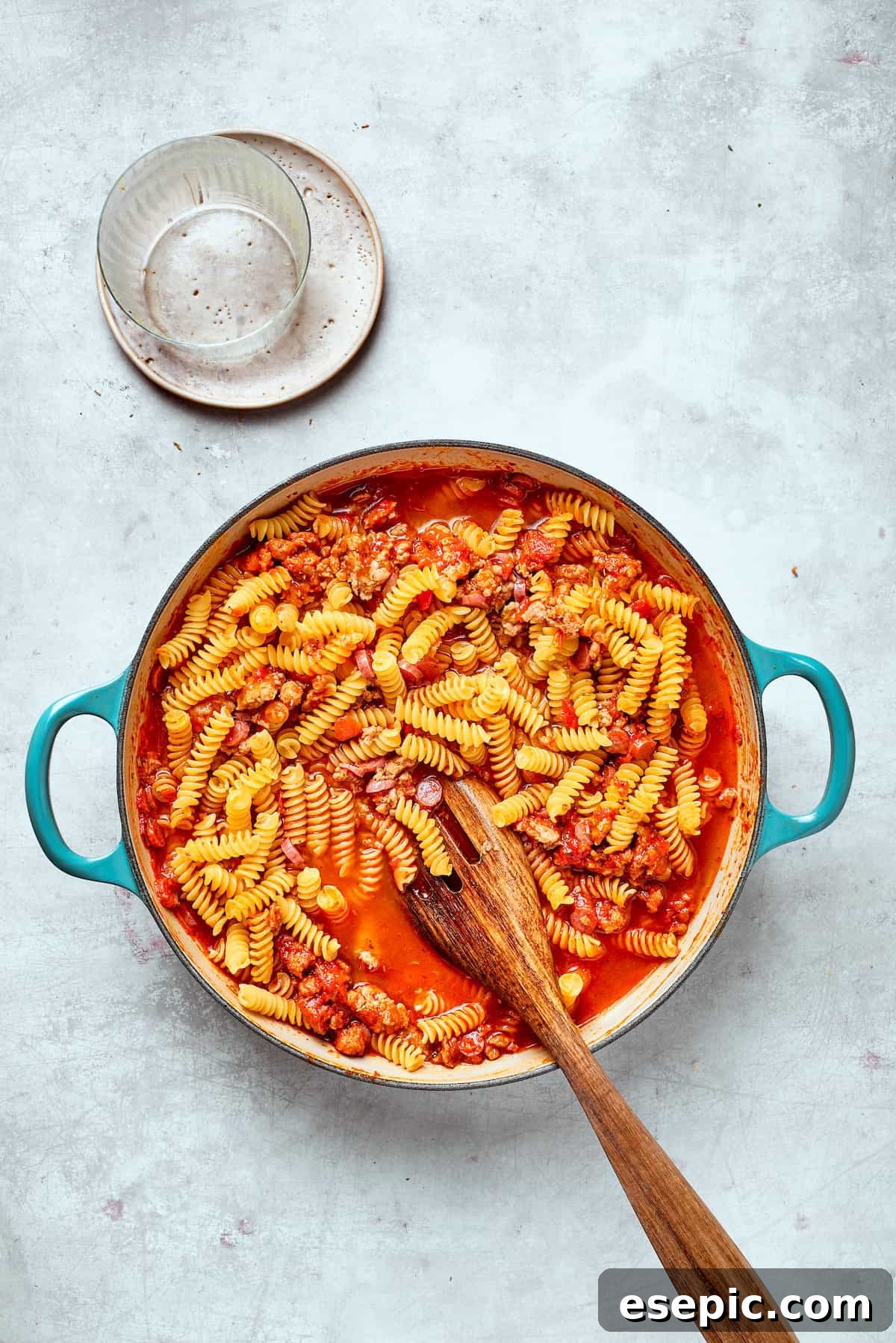 A spoon stirs the pasta into the sauce, ensuring it's fully coated.