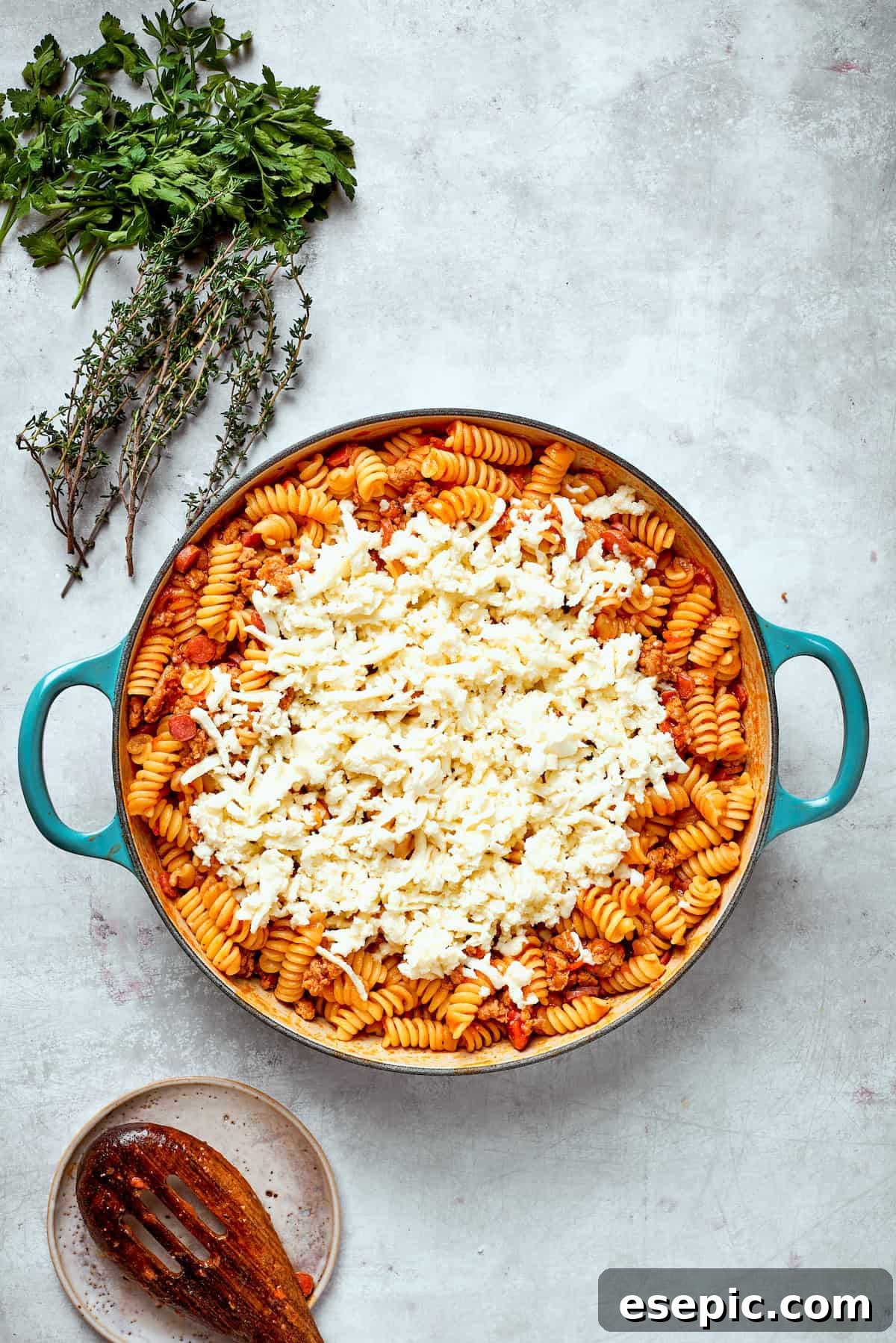 Cheese is added to a pan of pizza pasta, ready for melting.