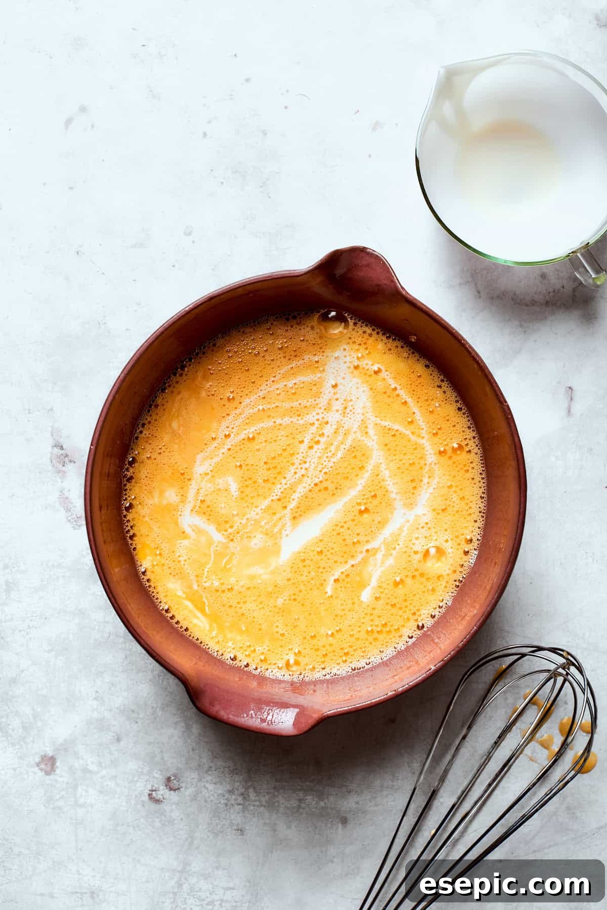 Eggs being whisked thoroughly with heavy cream and salt in a mixing bowl.