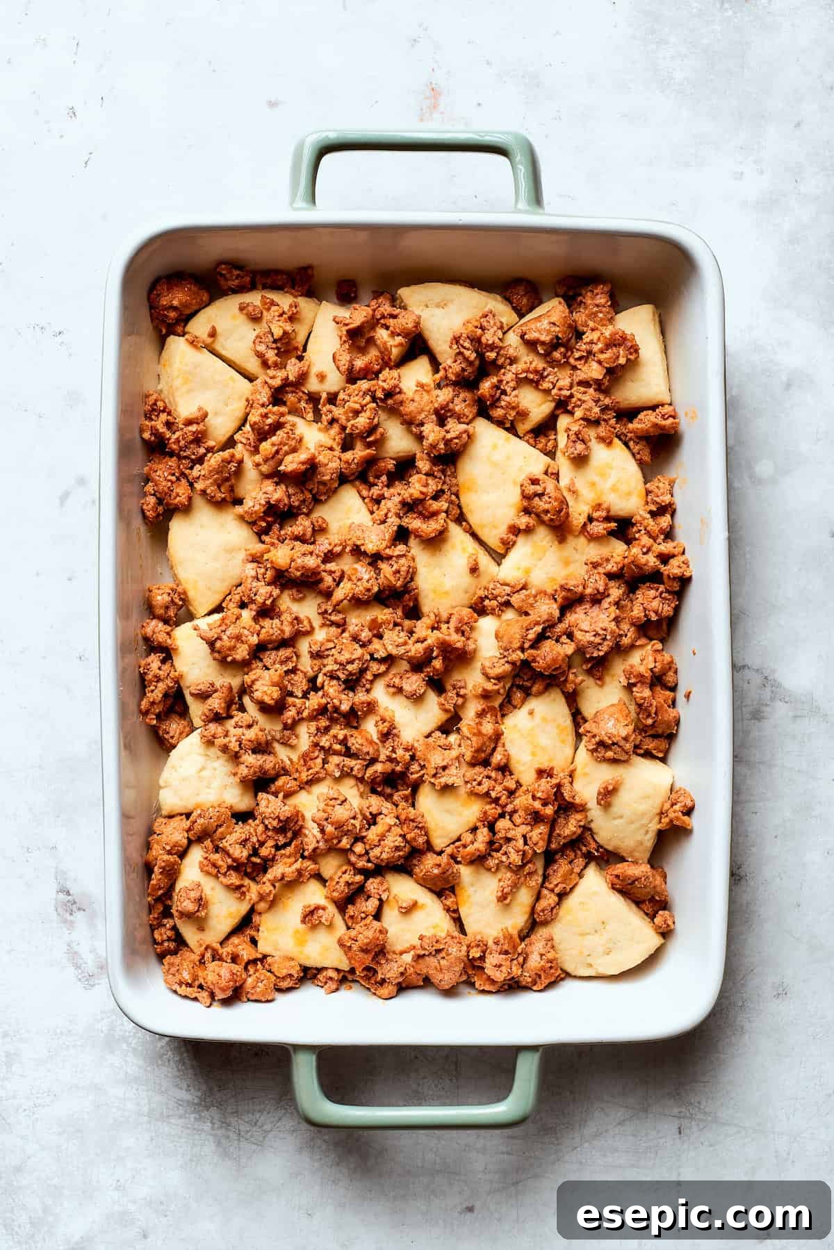Browned sausage crumbles spread evenly over the biscuit dough base in a baking pan.