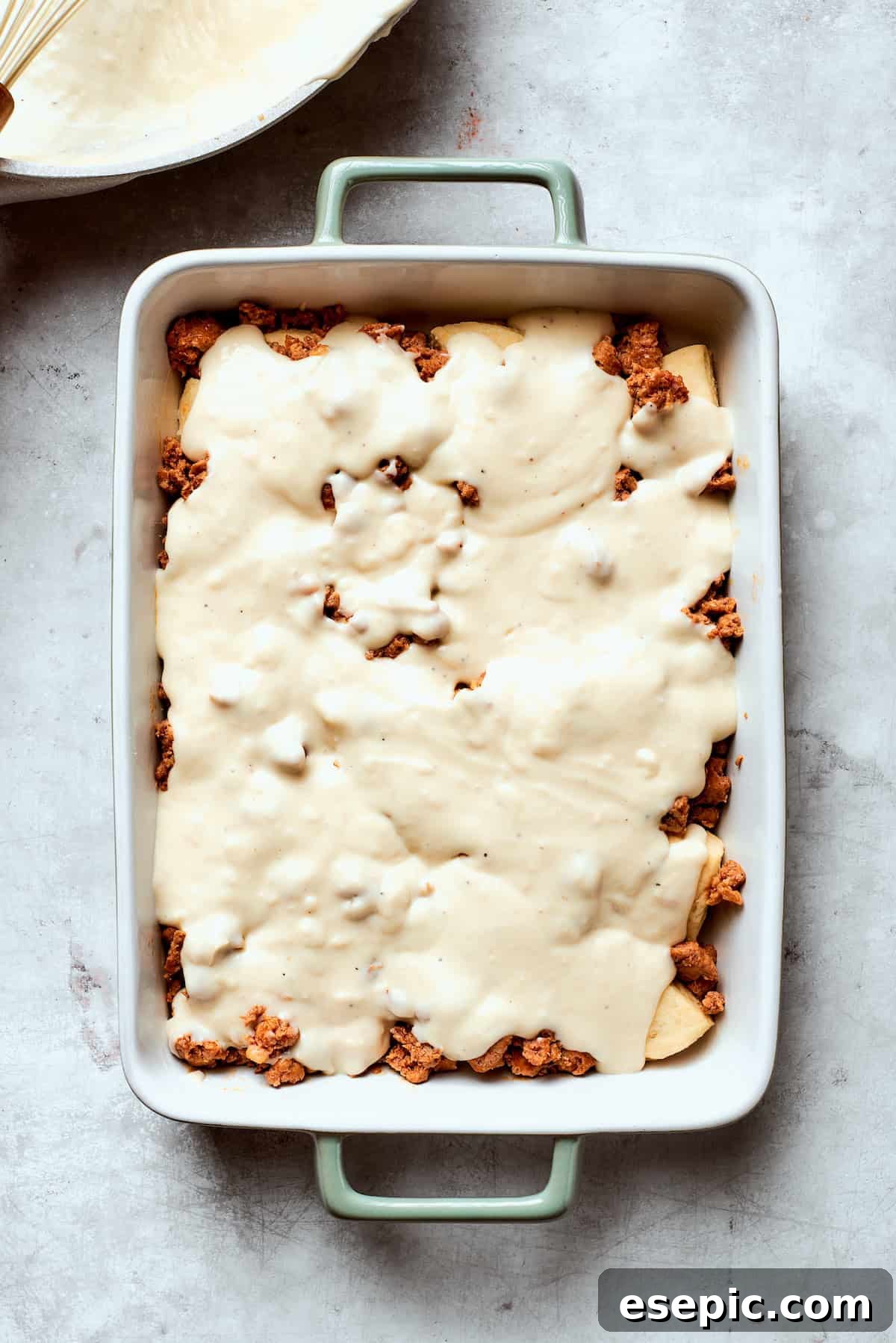 Thick, creamy gravy being poured generously over the sausage layer in the casserole dish.