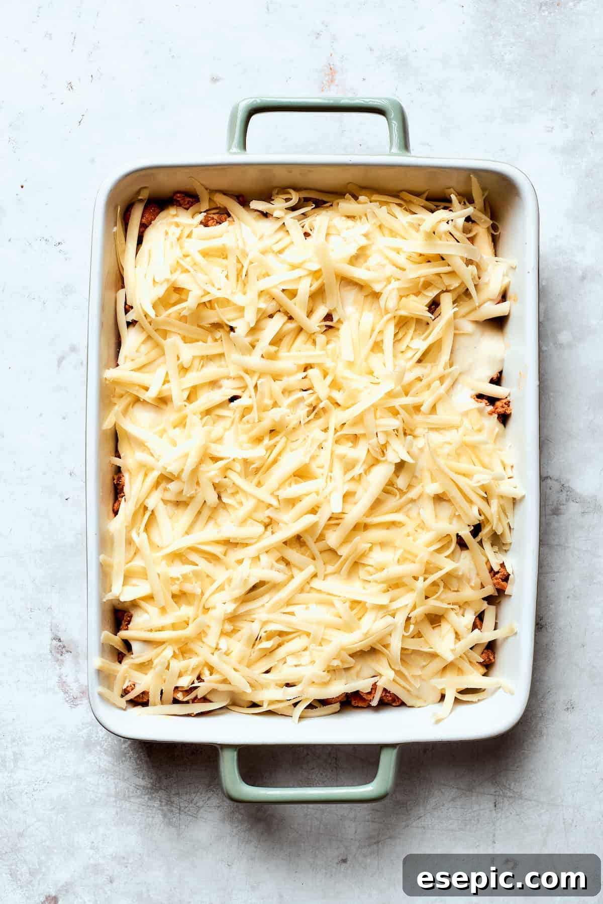 One cup of shredded Colby Jack cheese being sprinkled over the gravy layer in the casserole.