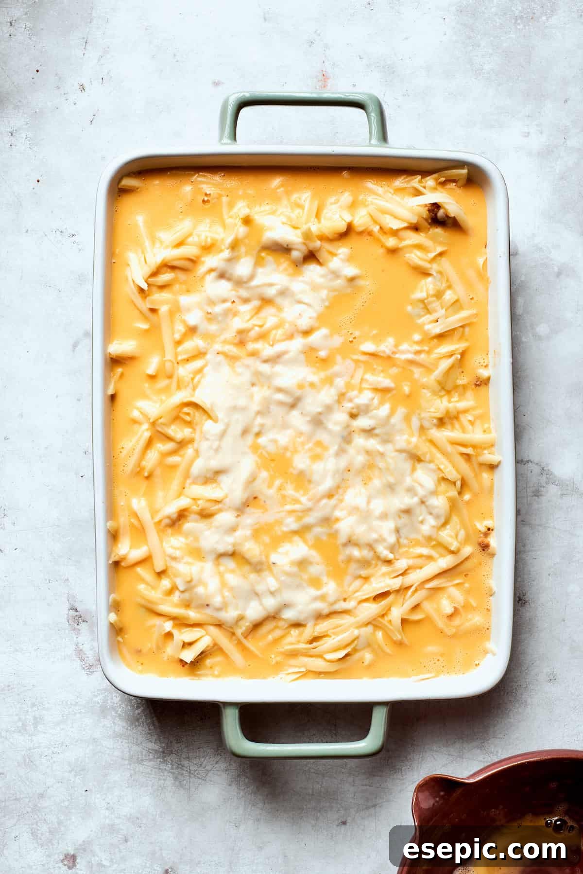 The whisked egg mixture being poured carefully over the cheese layer in the biscuits and gravy casserole.