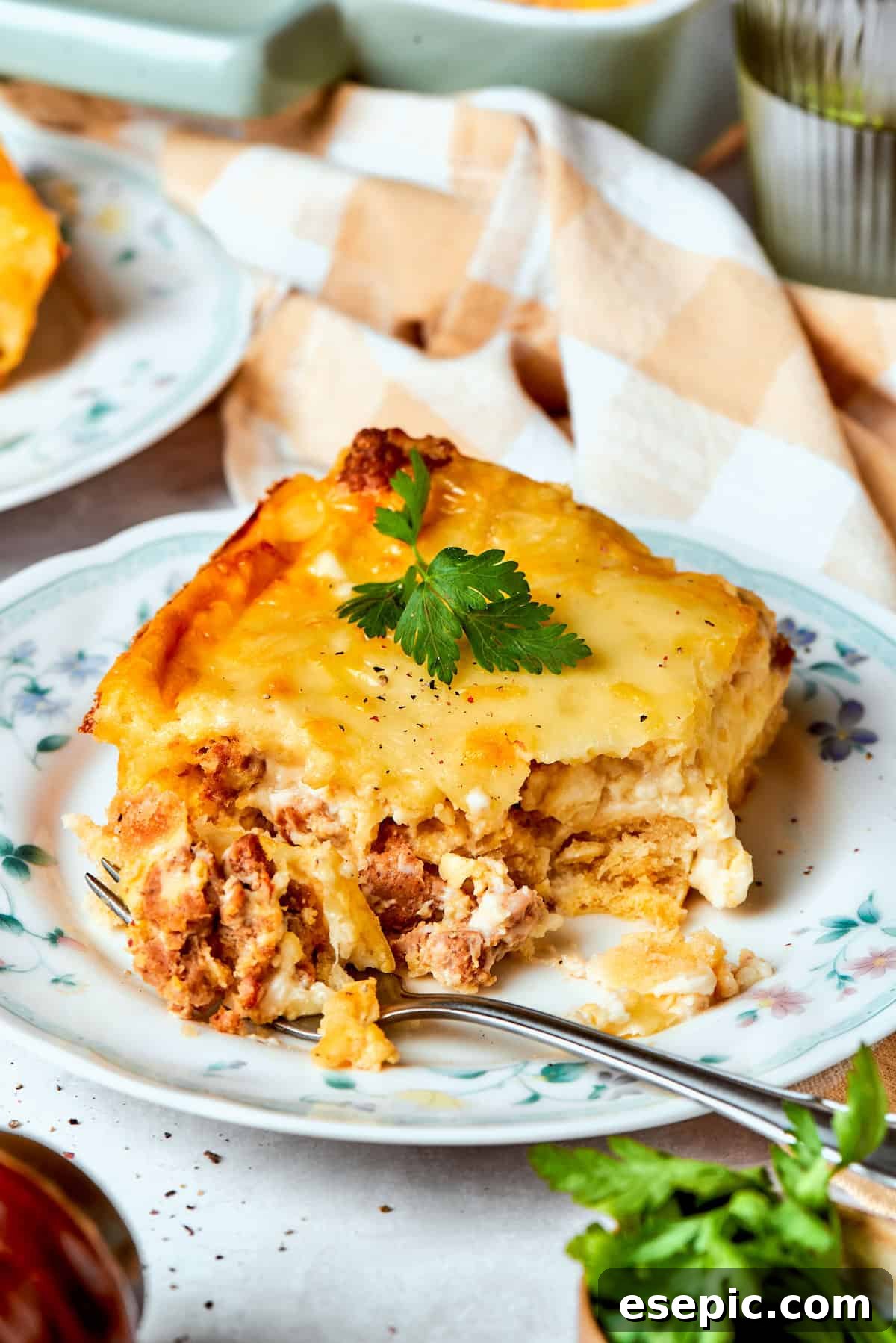 A fork cuts into a piece of biscuits and gravy casserole, highlighting the textures of the biscuit, gravy, and cheese layers.