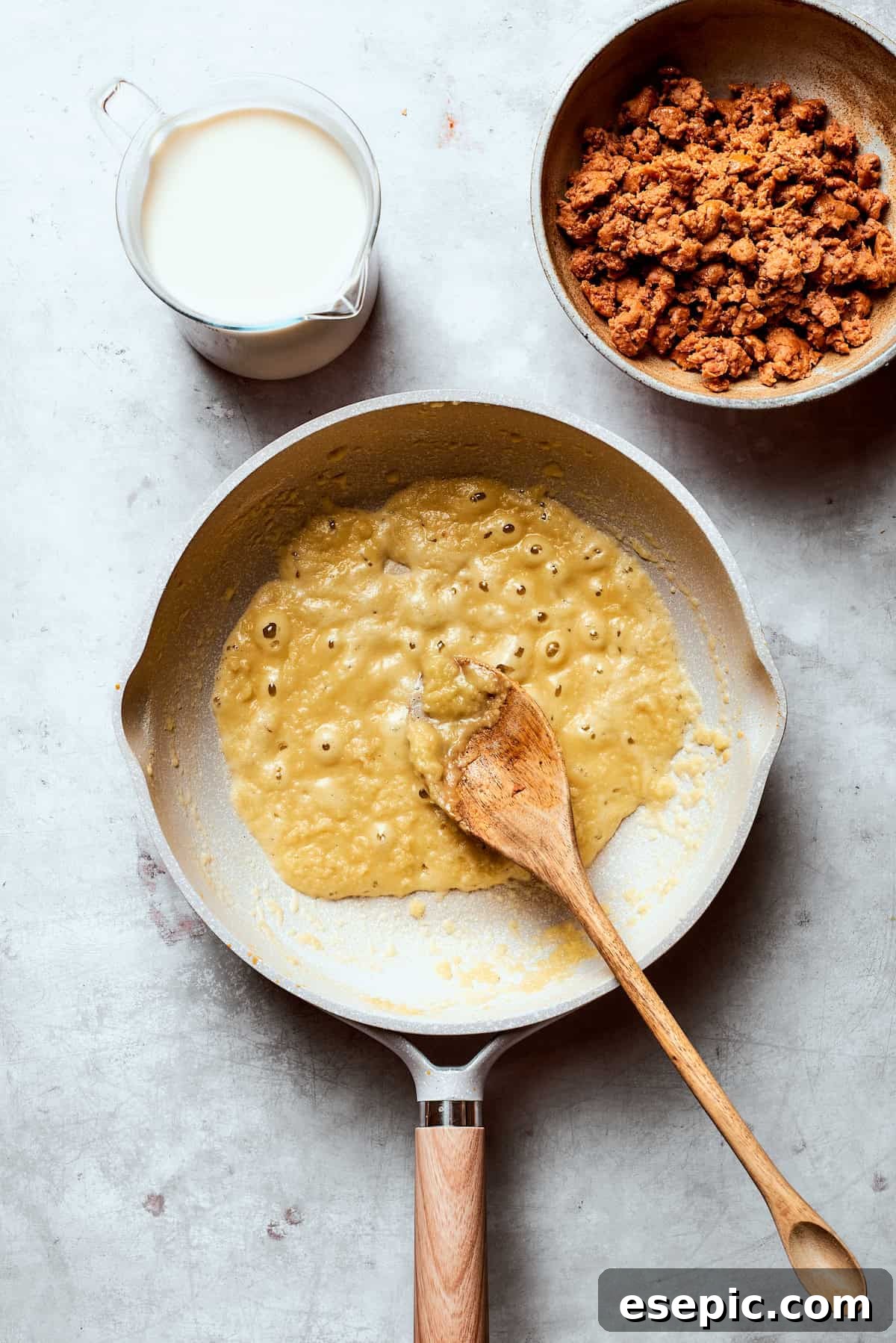 A roux being mixed and stirred constantly in a skillet, turning a light golden color.