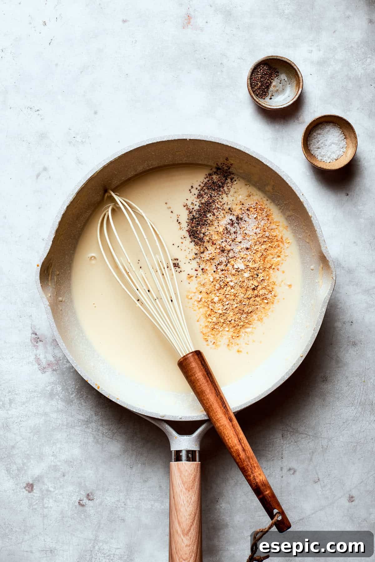 Seasonings (onion powder, salt, pepper) being added to the thickening gravy in a skillet.