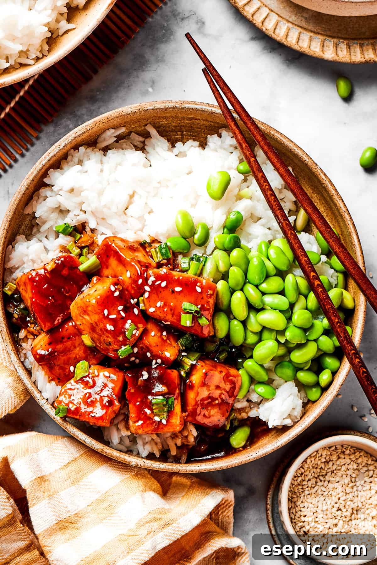 My teriyaki salmon recipe glazes flaky salmon with a homemade sticky-sweet marinade that adds tons of flavor. A bowl of white rice topped with cubed teriyaki salmon and vibrant green edamame, garnished with sesame seeds.