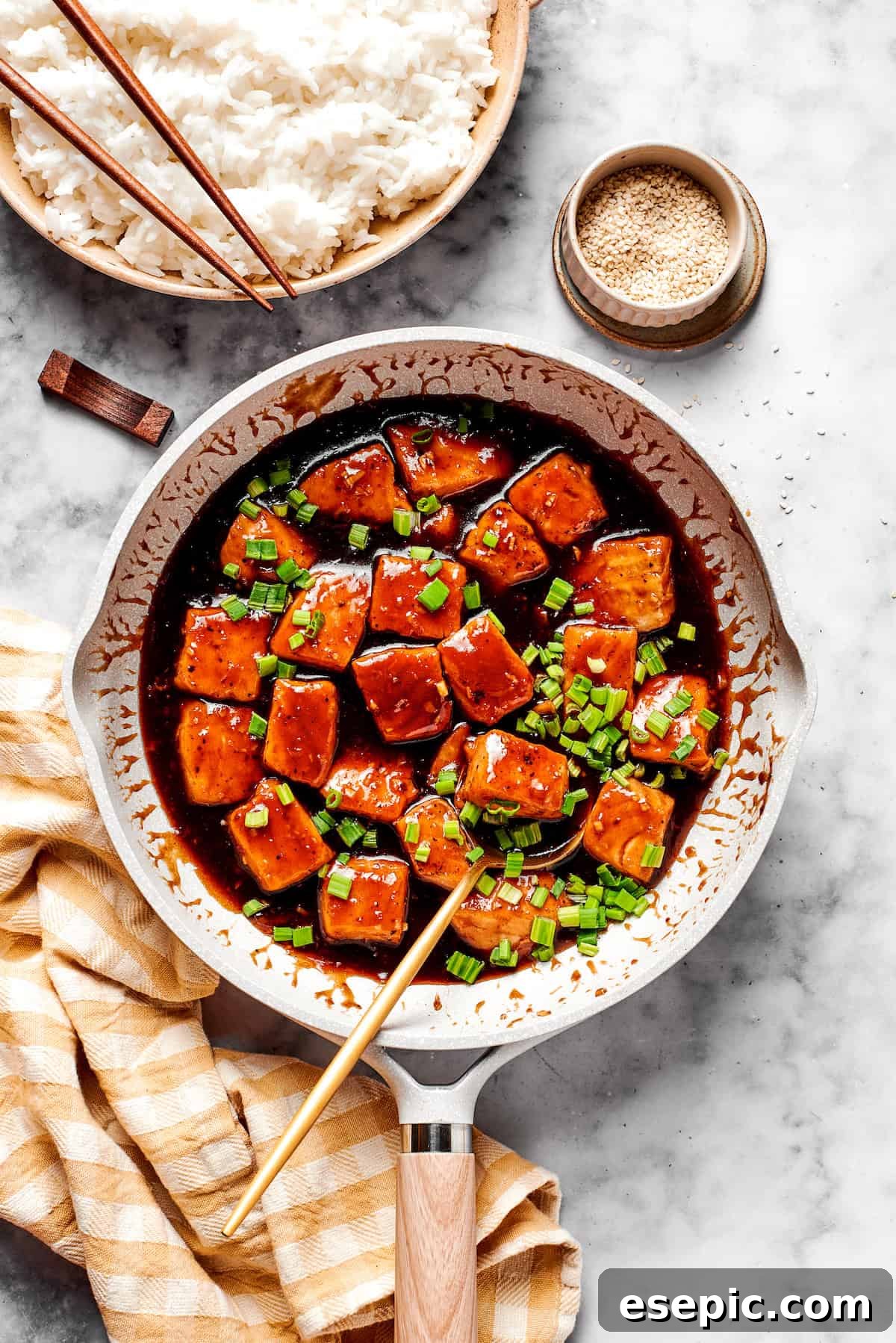My teriyaki salmon recipe glazes flaky salmon with a homemade sticky-sweet marinade that adds tons of flavor. A skillet full of cooked teriyaki salmon alongside a bowl of steaming white rice, ready for serving.