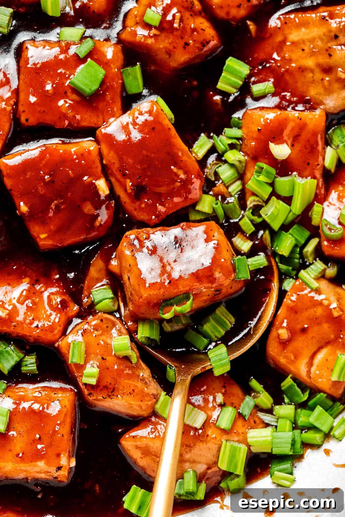 My teriyaki salmon recipe glazes flaky salmon with a homemade sticky-sweet marinade that adds tons of flavor. A close-up of teriyaki salmon in a bowl, with a spoon gently lifting a piece, highlighting its glossy glaze.