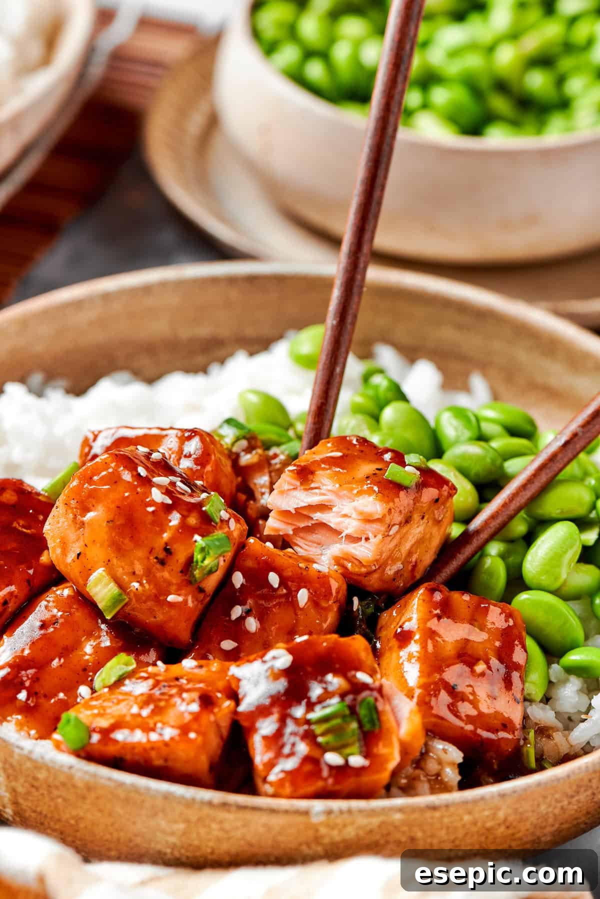 My teriyaki salmon recipe glazes flaky salmon with a homemade sticky-sweet marinade that adds tons of flavor. Chopsticks delicately picking up a piece of glazed teriyaki salmon, ready to be enjoyed.