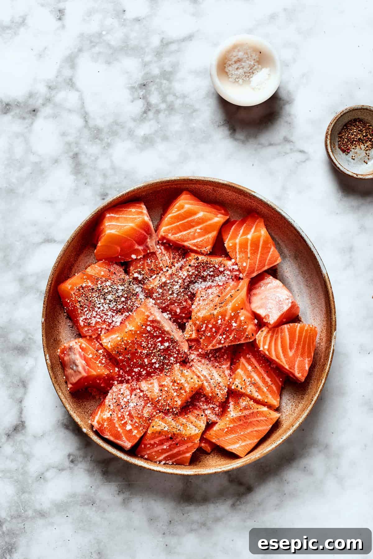 My teriyaki salmon recipe glazes flaky salmon with a homemade sticky-sweet marinade that adds tons of flavor. Cubed salmon fillets being seasoned generously with salt and pepper before cooking.