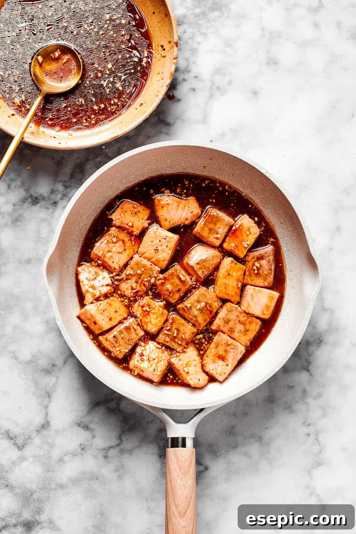 My teriyaki salmon recipe glazes flaky salmon with a homemade sticky-sweet marinade that adds tons of flavor. Teriyaki sauce being poured over cooked salmon cubes in a skillet, coating them in a rich glaze.