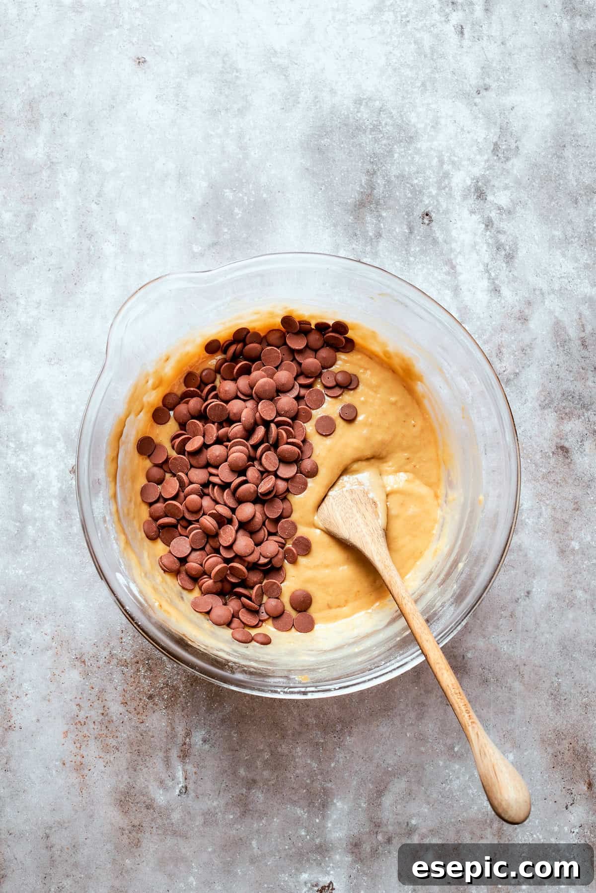 Chocolate chips are added to a bowl of banana bread batter.