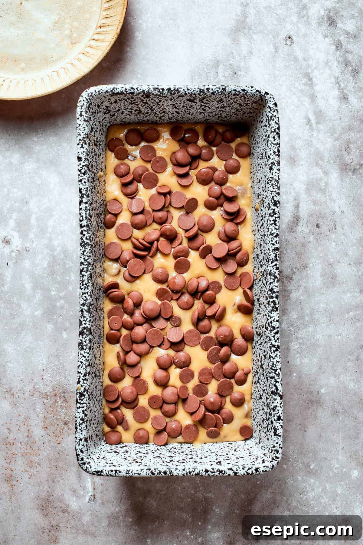 Banana chocolate chip bread in a loaf pan topped with chocolate chips.