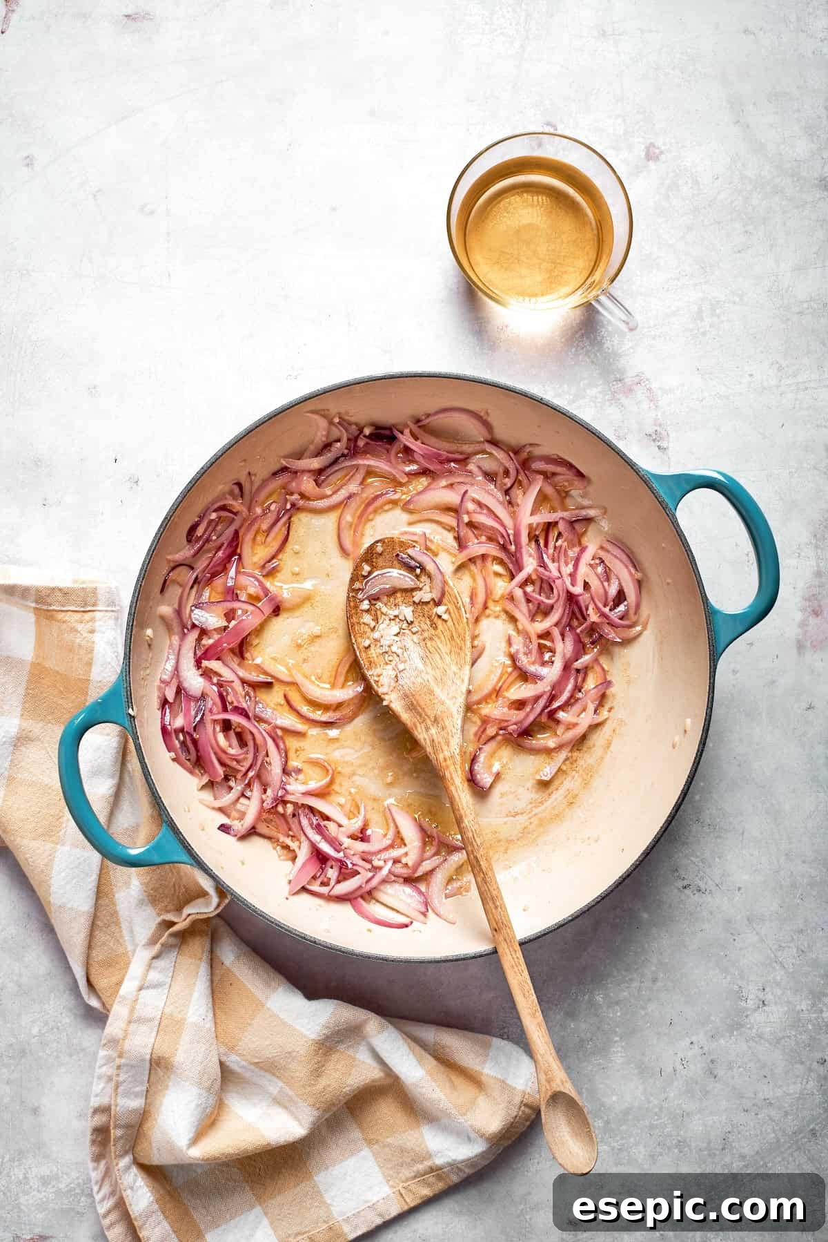 Cheesy, marry me chicken pasta features tender bites of chicken swirled in a creamy sauce along with sundried tomatoes and pasta. A spoon stirs a skillet of cooking onions and garlic.