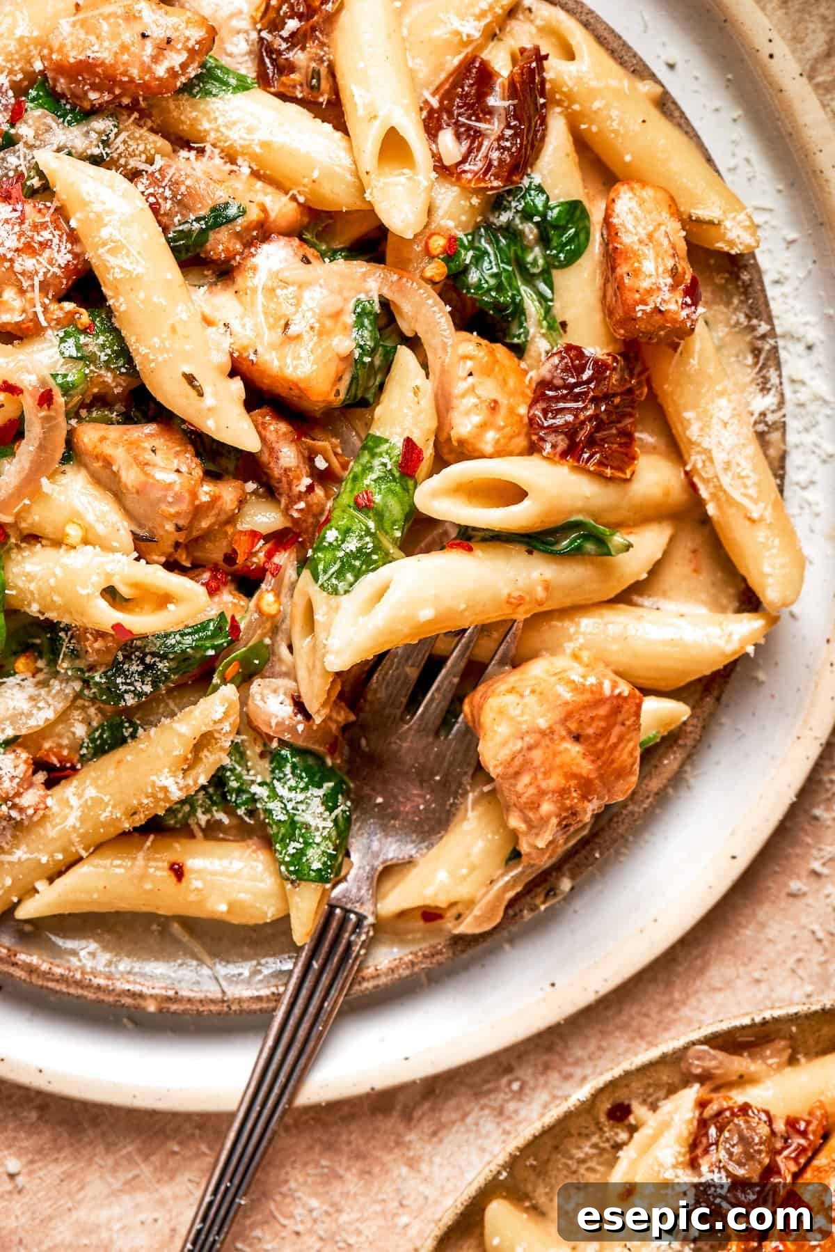 Cheesy, marry me chicken pasta features tender bites of chicken swirled in a creamy sauce along with sundried tomatoes and pasta. A fork rests in a plate of marry me chicken pasta.
