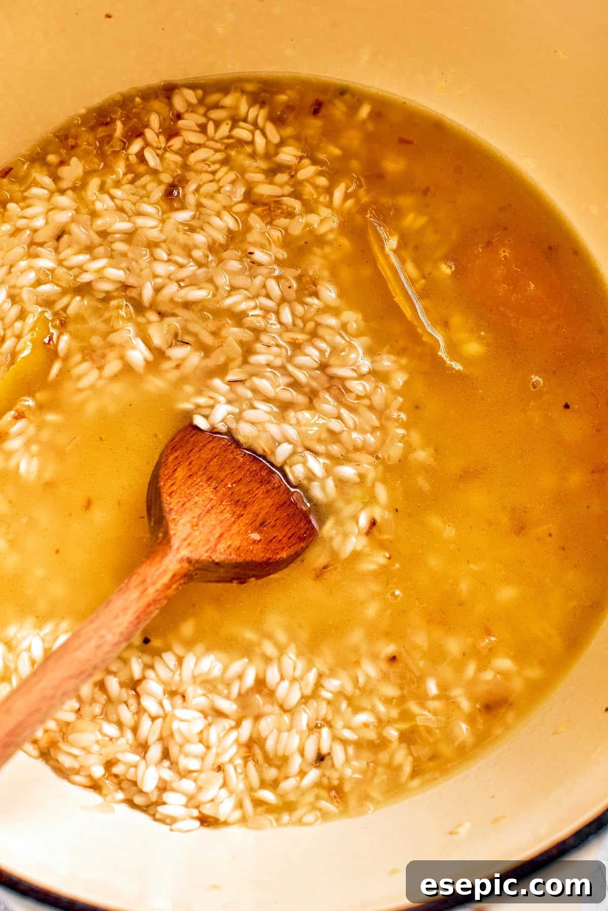 Ladlefuls of warm broth being stirred into the risotto rice, gradually absorbing into the grains.
