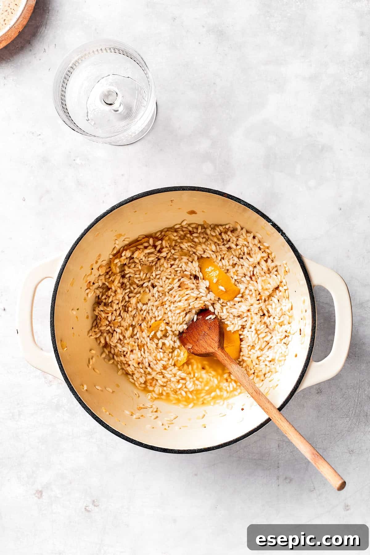 Pouring dry white wine into the pot with toasted rice and aromatics, stirring to deglaze.