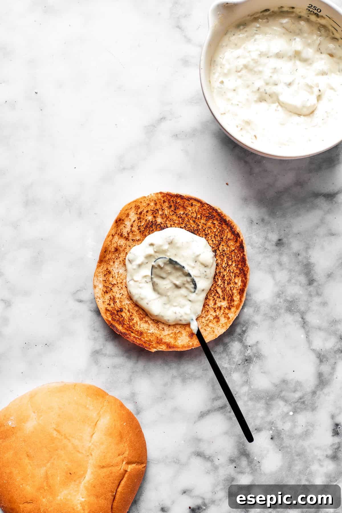 Tartar sauce is spread on a toasted bun.