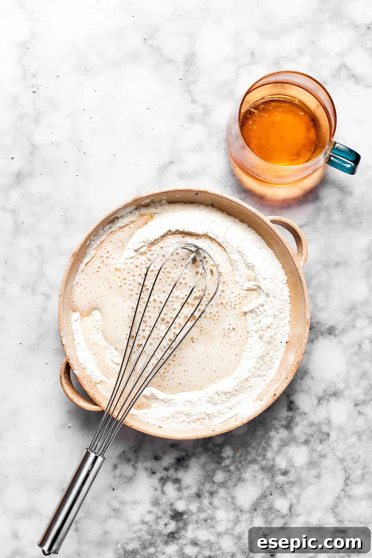 A whisk stirs a bowl of beer batter.