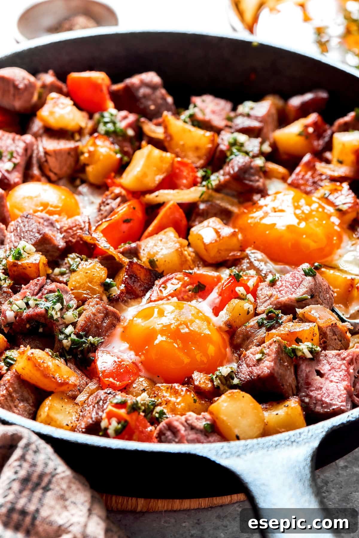 Fried eggs perfectly cooked on top of a pan of steak and eggs hash.