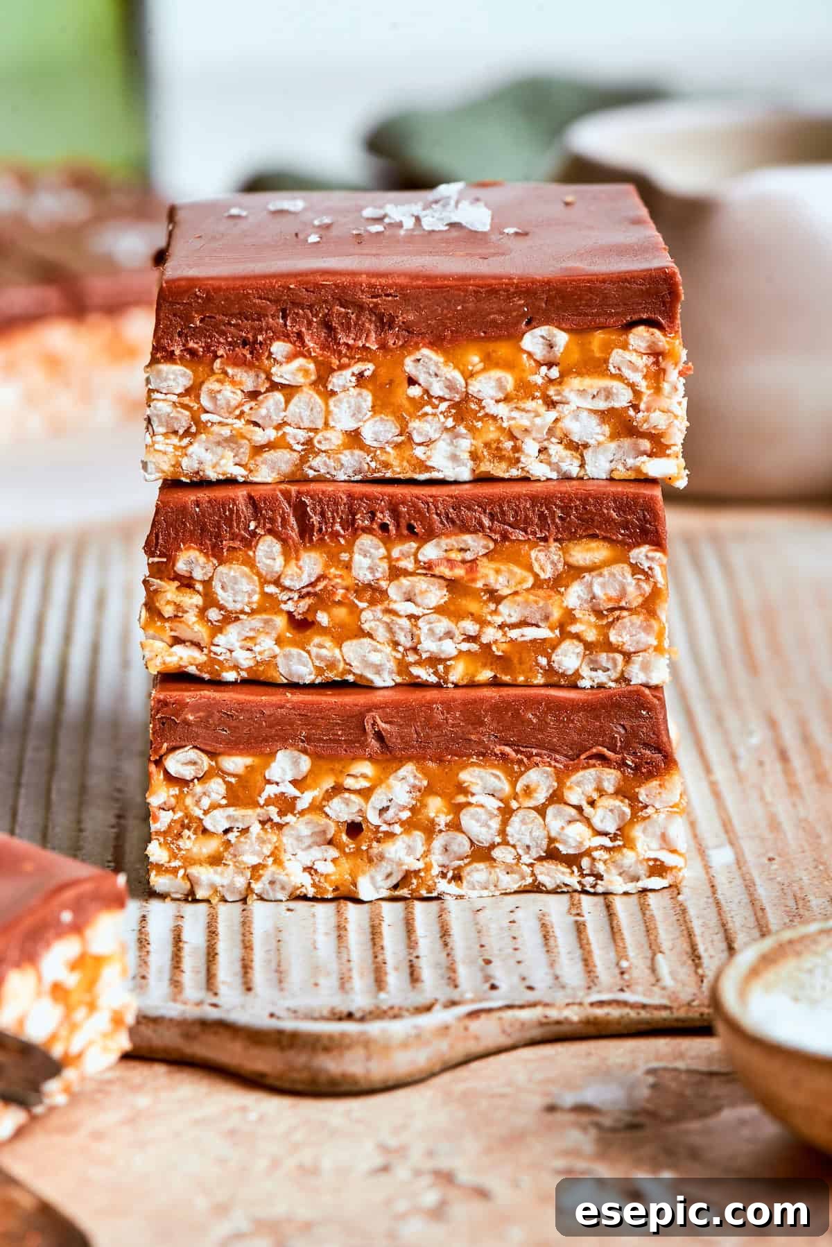 No-bake scotcharoos feature creamy peanut butter, crispy rice cereal, and a sweet layer of melted chocolate and butterscotch. Three scotcharoos stacked on top of each other, showcasing their layers.