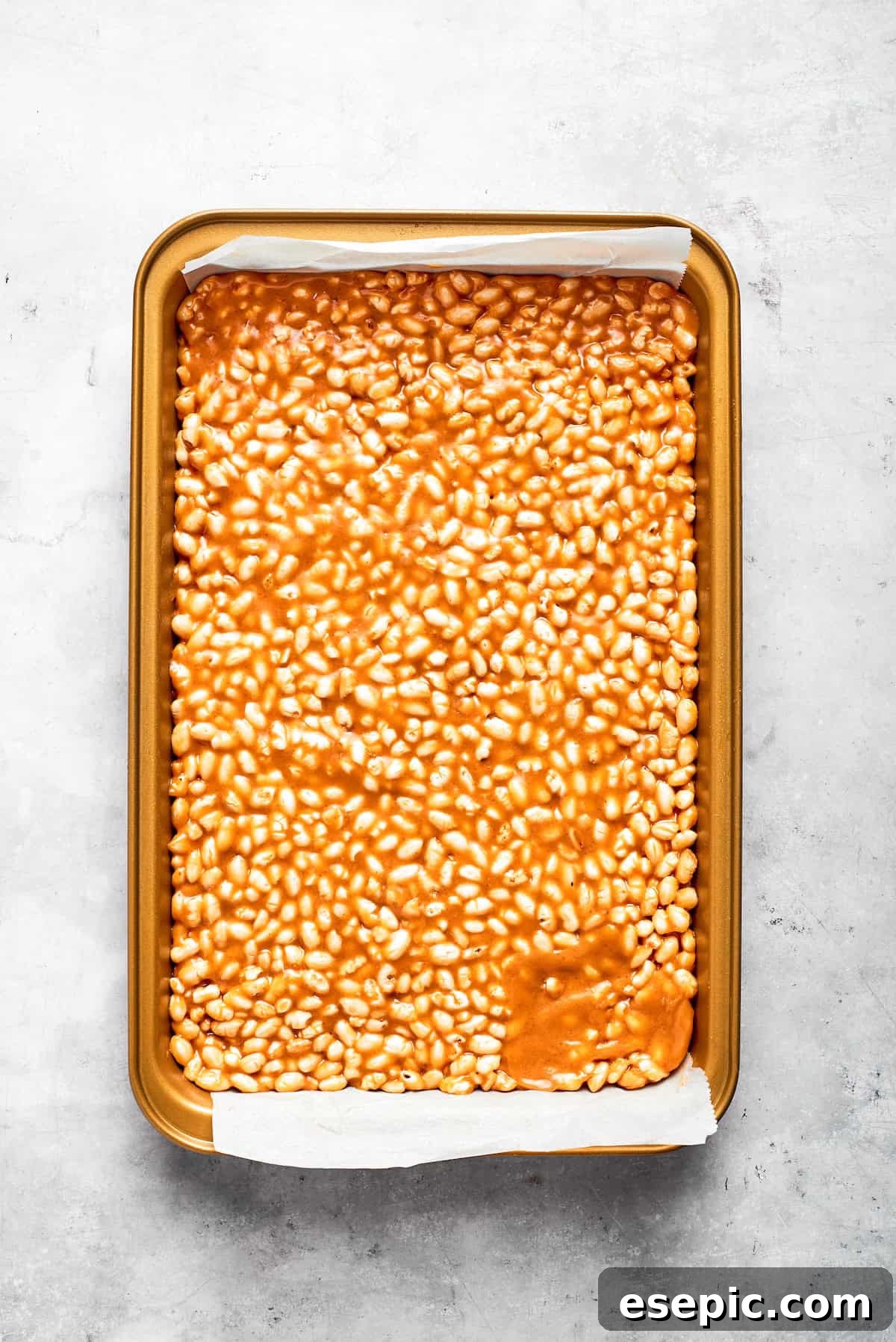 No-bake scotcharoos feature creamy peanut butter, crispy rice cereal, and a sweet layer of melted chocolate and butterscotch. Scotcharoos base firmly pressed into a baking pan, ready for topping.