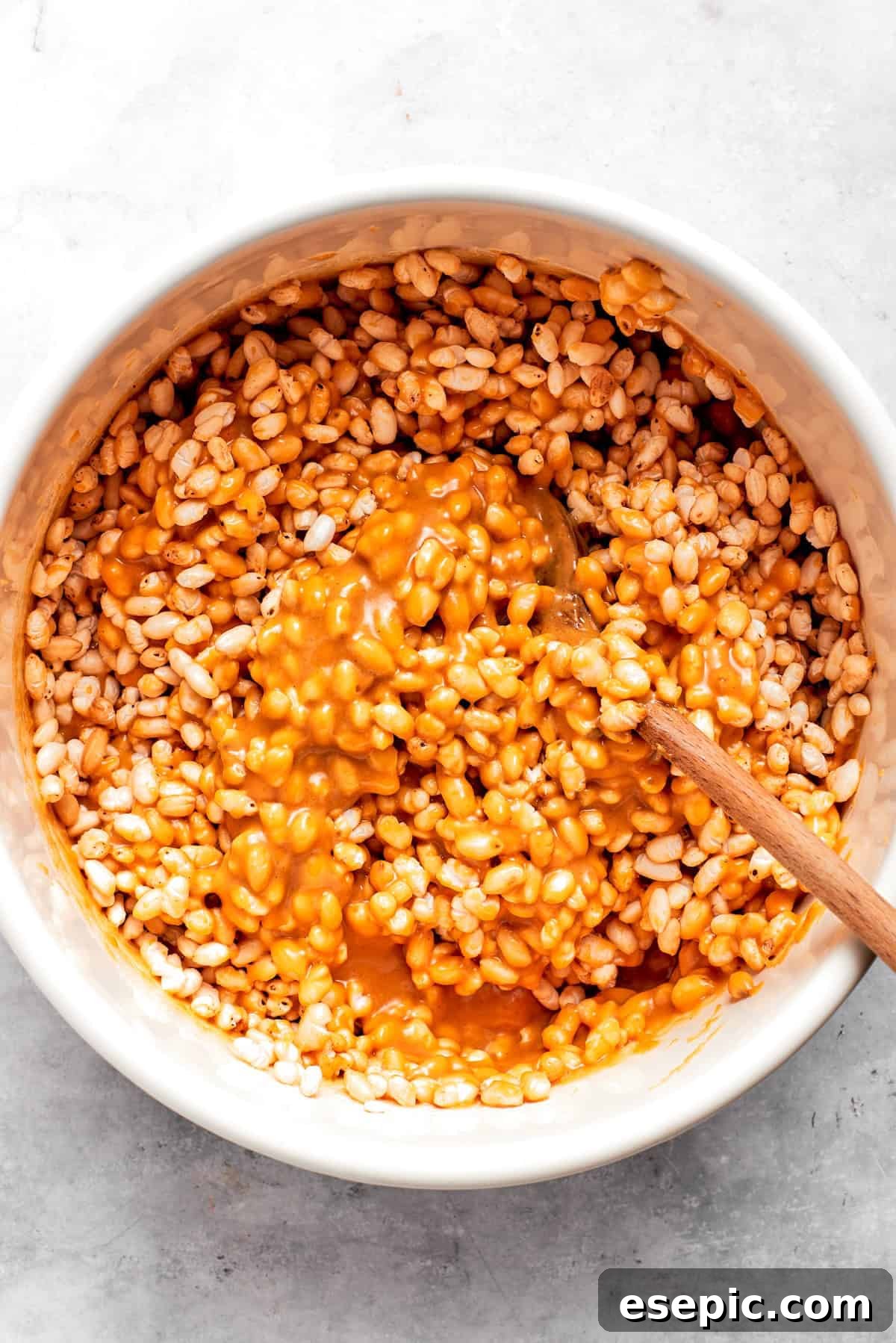 No-bake scotcharoos feature creamy peanut butter, crispy rice cereal, and a sweet layer of melted chocolate and butterscotch. Peanut butter mixture being incorporated into crispy rice cereal in a large bowl.