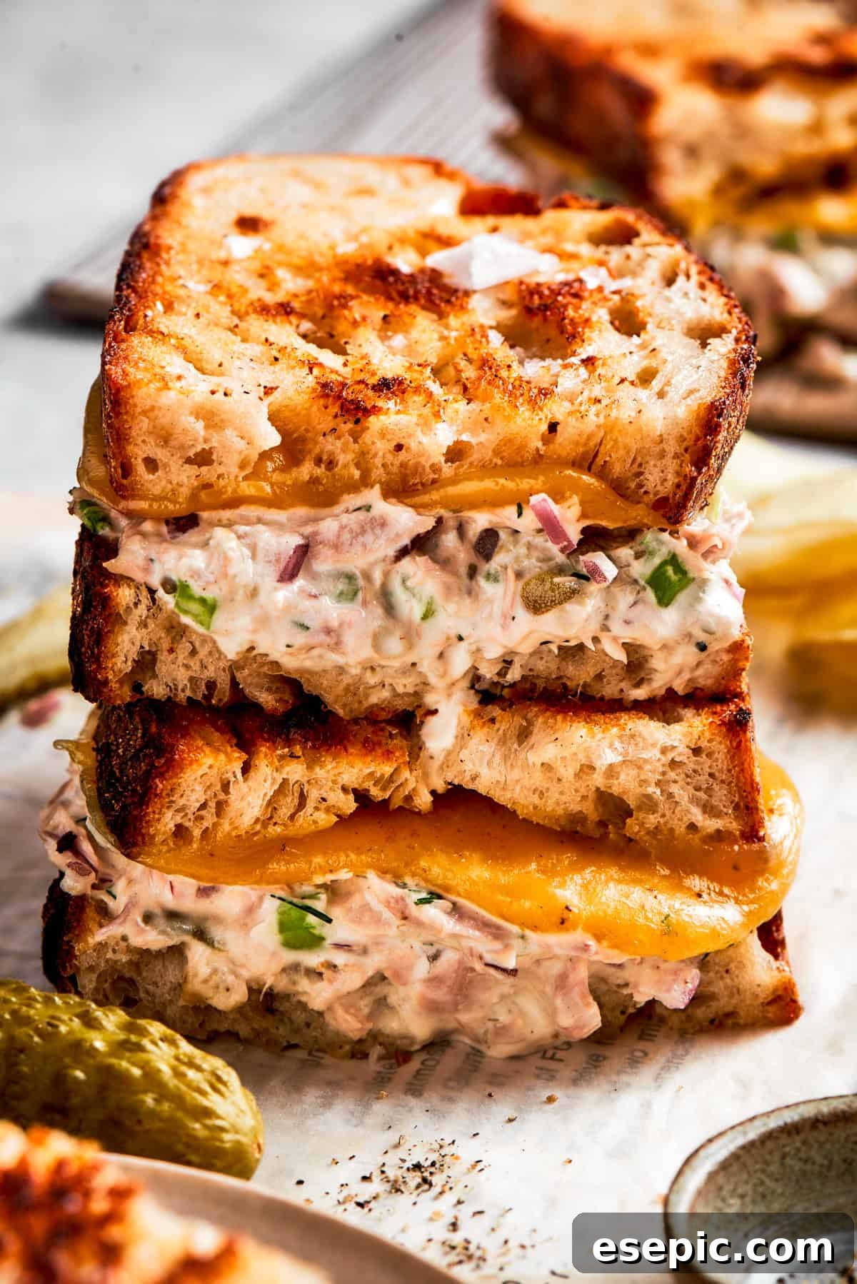 This toasty tuna melt recipe features a blend of creamy tuna salad and melty cheese stuffed between slices of sourdough and pan-fried to a crisp. Two halves of tuna melt stacked on top of each other, showcasing melted cheese and creamy tuna filling.