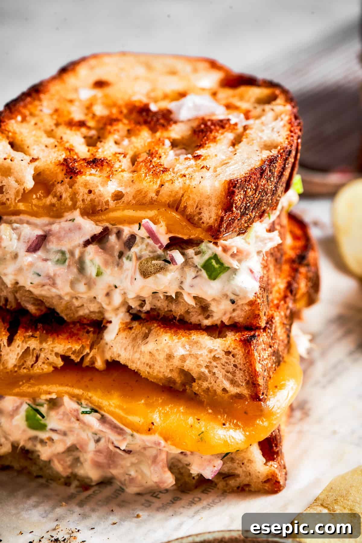 This toasty tuna melt recipe features a blend of creamy tuna salad and melty cheese stuffed between slices of sourdough and pan-fried to a crisp. A close-up shot of two tuna melt sandwiches stacked, highlighting the crisp sourdough bread, melted cheddar cheese, and rich tuna salad filling.