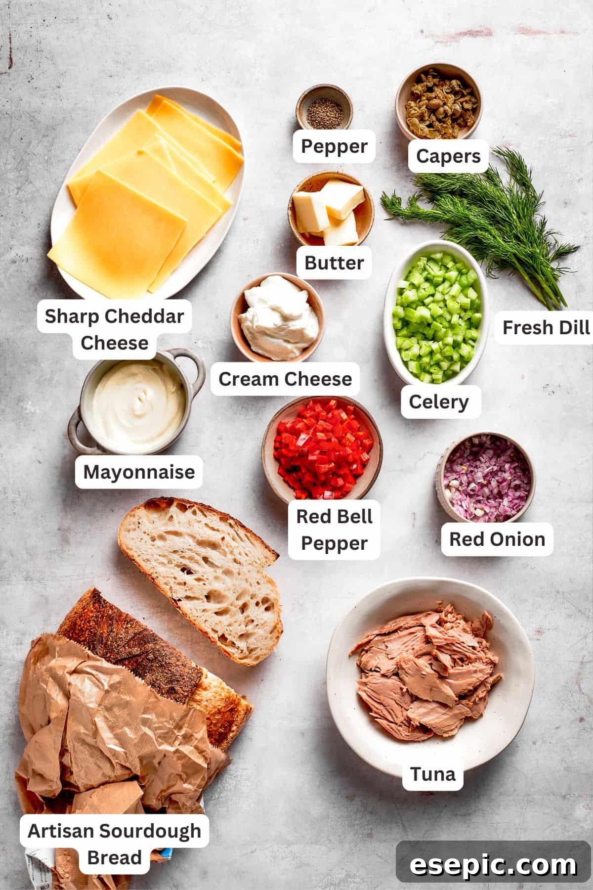 This toasty tuna melt recipe features a blend of creamy tuna salad and melty cheese stuffed between slices of sourdough and pan-fried to a crisp. Ingredients for a tuna melt recipe are text-labeled, including red onion, celery, bell pepper, mayo, cream cheese, dill, capers, tuna, pepper, butter, bread, and cheese.