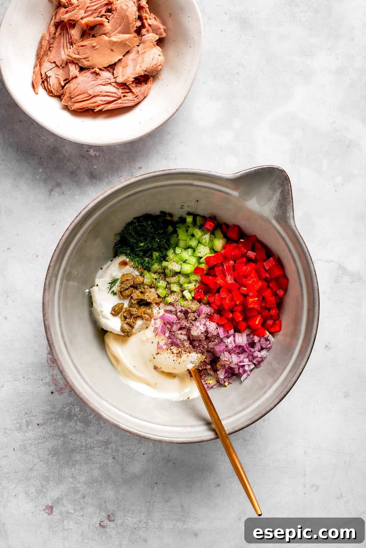 This toasty tuna melt recipe features a blend of creamy tuna salad and melty cheese stuffed between slices of sourdough and pan-fried to a crisp. Finely chopped vegetables (red onion, celery, red bell pepper) and creamy ingredients (mayonnaise, cream cheese, dill, capers) in a mixing bowl for tuna melt filling.
