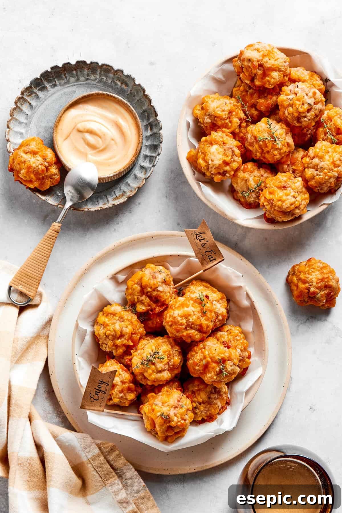 This sausage balls recipe relies on Bisquick, pork sausage, and Italian seasoning for an easy appetizer. Don't forget the dipping sauce! Two bowls overflowing with hot, cheesy sausage balls, accompanied by a small bowl of creamy dipping sauce and a spoon, ready to be enjoyed.