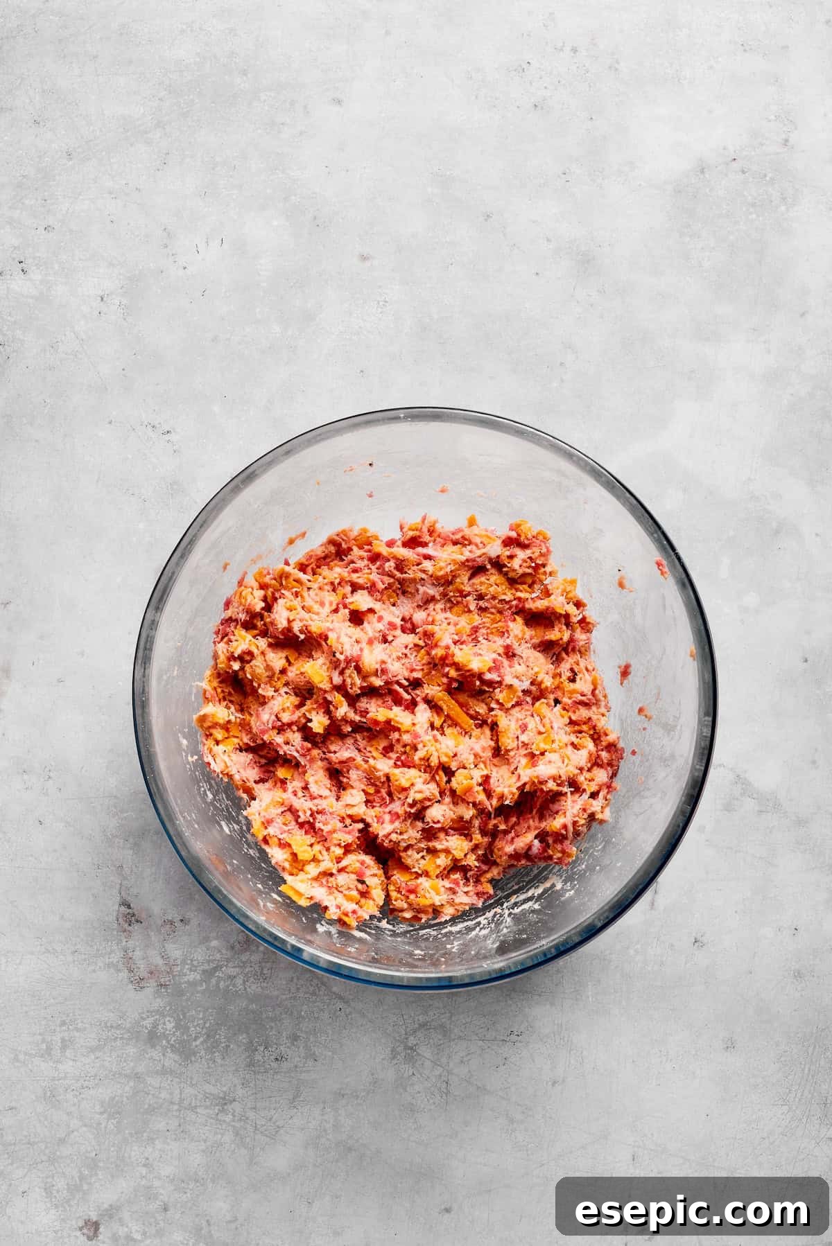 This sausage balls recipe relies on Bisquick, pork sausage, and Italian seasoning for an easy appetizer. Don't forget the dipping sauce! The sausage ball mixture is being thoroughly combined in a glass bowl, showcasing the uniform blend of sausage, cheese, and biscuit mix.