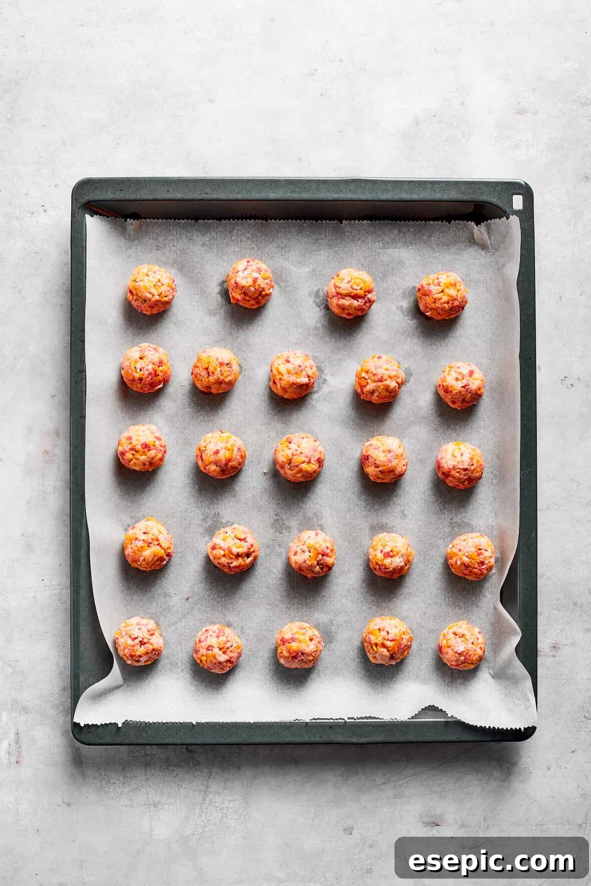 This sausage balls recipe relies on Bisquick, pork sausage, and Italian seasoning for an easy appetizer. Don't forget the dipping sauce! Small, uniformly shaped sausage balls are neatly arranged on a parchment-lined baking sheet, ready for baking.